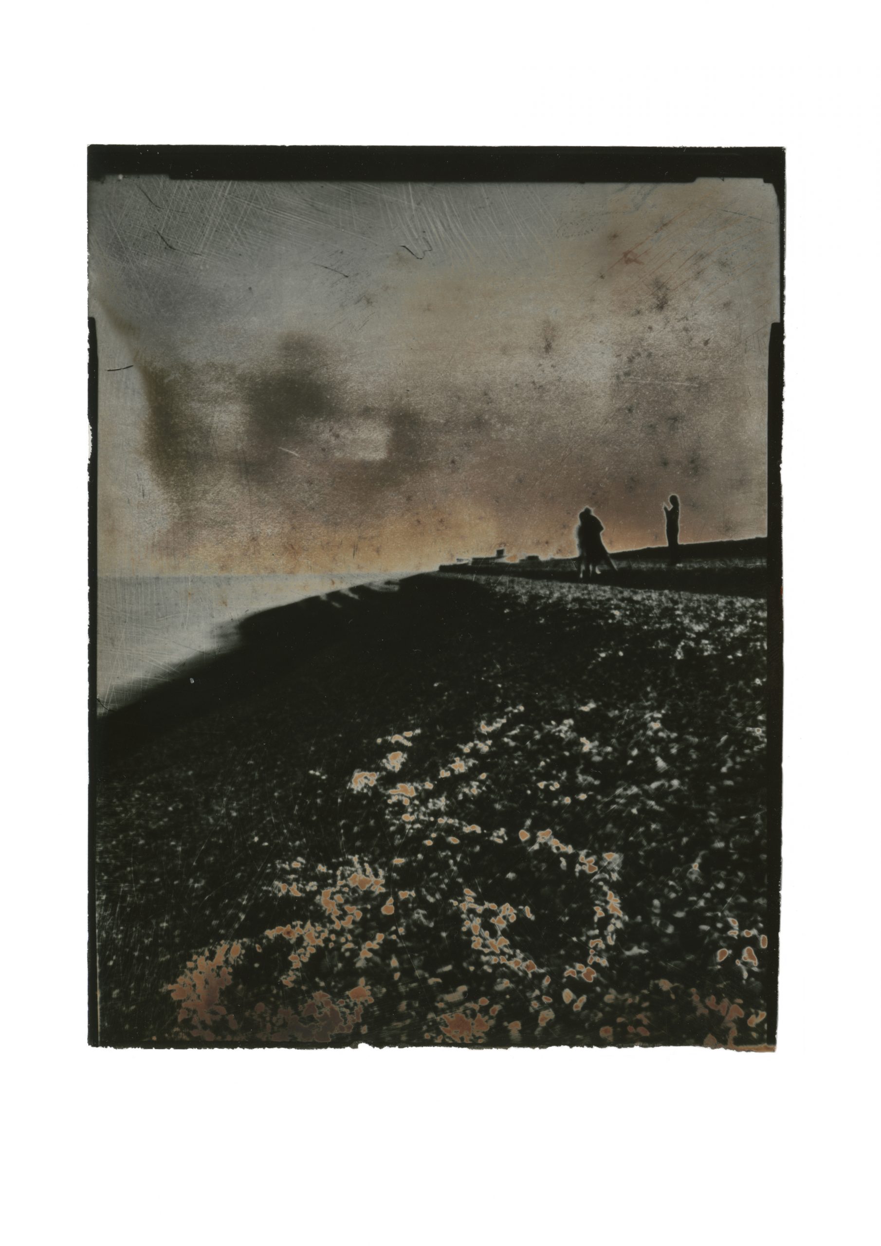 brooding contrasty image of steep bank of shingle with handprinted sky horizon line punctuated by shout of two figures